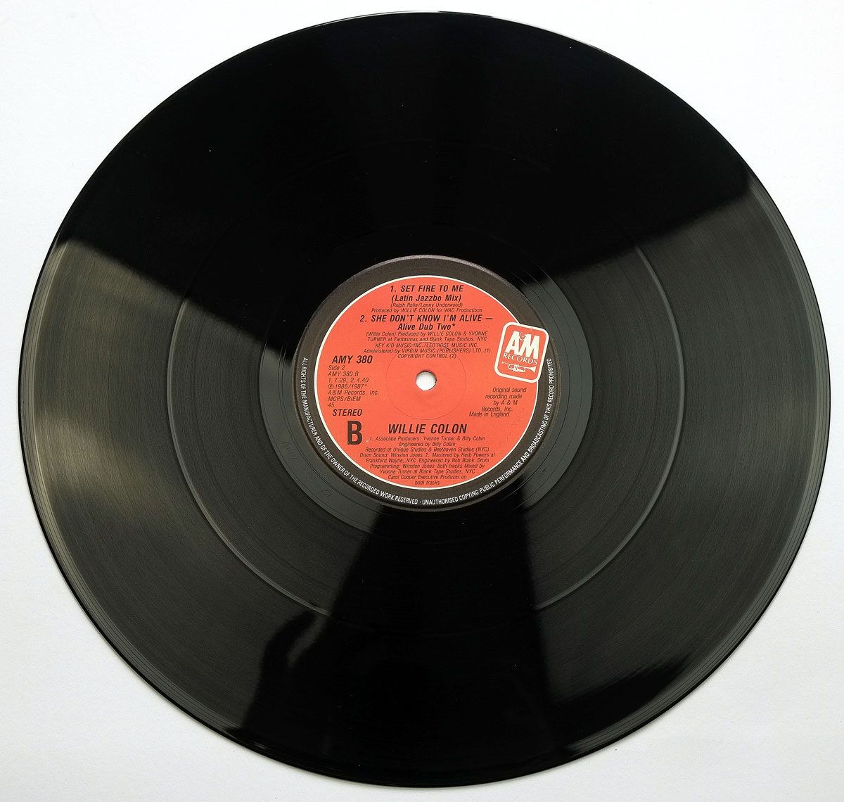 Full view of Side B of the 1987 UK 12-inch vinyl EP 'She Don't Know I'm Alive' by Willie Colón, showing a red A&M label with tracks 'Set Fire to Me (Latin Jazzbo Mix)' and 'Alive Dub Two', catalog number AMY 380, and stereo format.